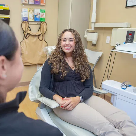 Female patient smiling while sitting in dental chair during consultation with dentist in office.