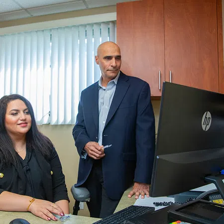 Two professionals in business attire working together at a computer in an office setting with wooden cabinets.