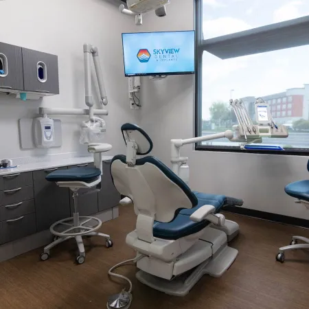 Modern dental office with a blue dental chair, equipment, and SkyView Dental logo on wall monitor