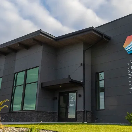 Modern gray building exterior with large windows and Skyview Dental & Implants logo on walls under a cloudy sky.