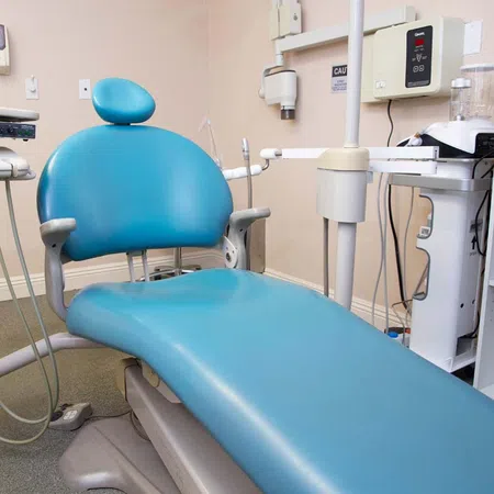 Blue dental chair with attached equipment in a clean dental clinic room ready for patient care