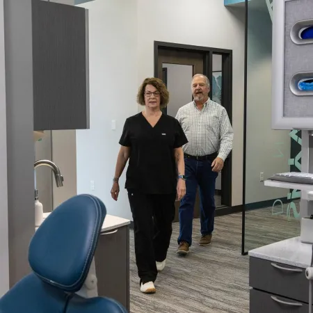 Dental office interior with a female dental professional and male patient walking through modern treatment area.