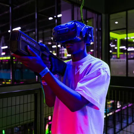 Person wearing VR headset and holding a futuristic game gun in neon-lit indoor gaming arena at night