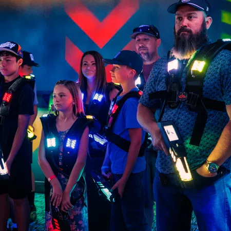 Group of people wearing glowing vests and holding laser tag guns inside a neon-lit arena.