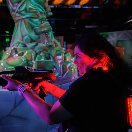 Young woman playing laser tag aiming a gun in a neon-lit indoor arena with futuristic decor.