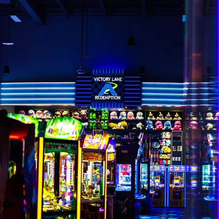 Brightly lit arcade redemption game area with plush toys and colorful machines under Victory Lane sign.