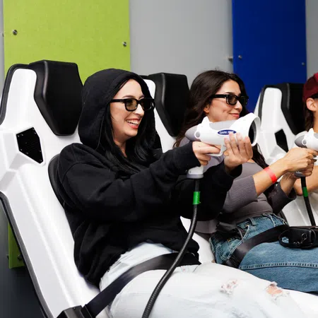 Four people seated in VR chairs wearing 3D glasses, holding VR controllers, and engaging in a virtual reality game experience.