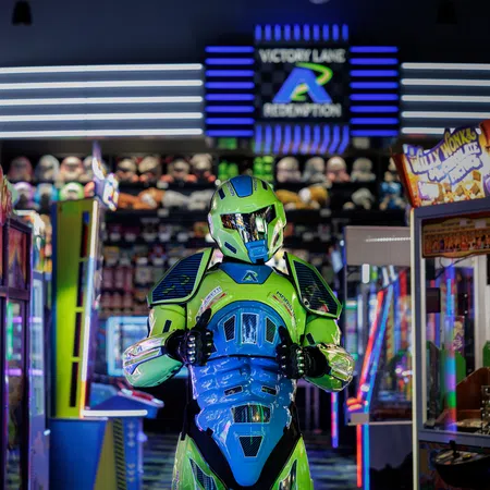 Person in bright green and blue futuristic armor costume standing inside a colorful arcade center.