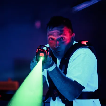 Man playing laser tag aiming green laser gun in dark room with glowing gear and focused expression