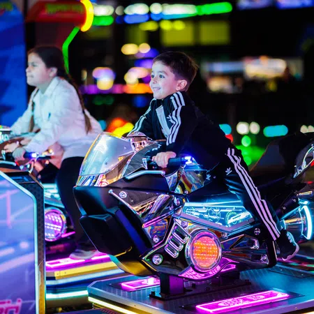 Two children enjoying a glowing motorcycle arcade game with vibrant neon lights in a gaming arcade.
