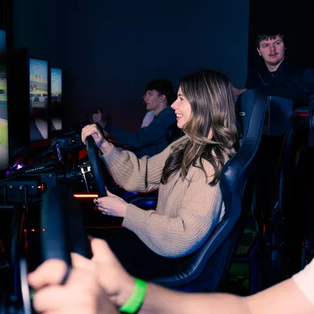 Group of people playing a realistic driving racing simulator game with steering wheels and large screens in a dark room