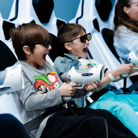 Children wearing 3D glasses and holding toy guns enjoy an interactive arcade shooting game.