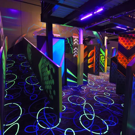 Vibrant laser tag arena with neon walls and glowing floor designs under black light.