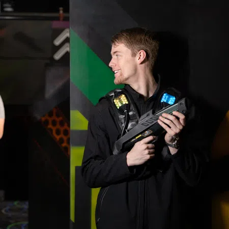 Two players in a laser tag arena, one hiding and the other aiming, showcasing excitement and teamwork.