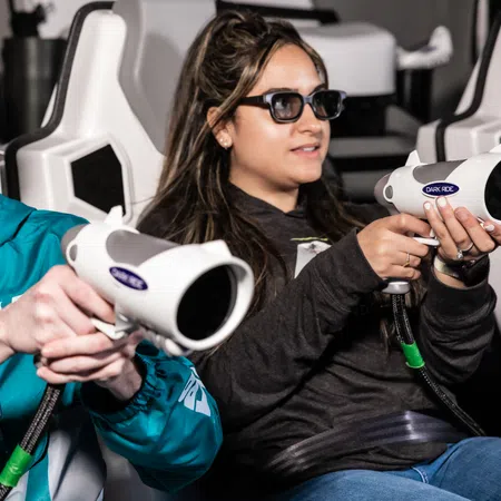 Two people wearing 3D glasses engage in an interactive gaming experience, holding futuristic controllers.