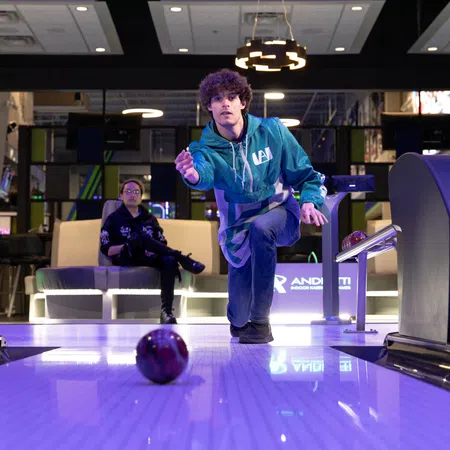 A young bowler in a green hoodie prepares to roll a bowling ball down the lane at an entertainment center.