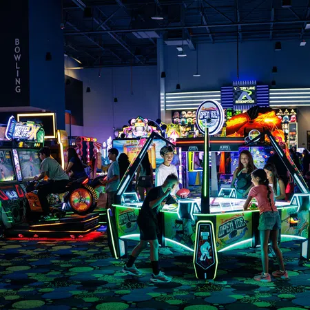 Children and teens playing air hockey and arcade games in a vibrant, neon-lit indoor arcade center.