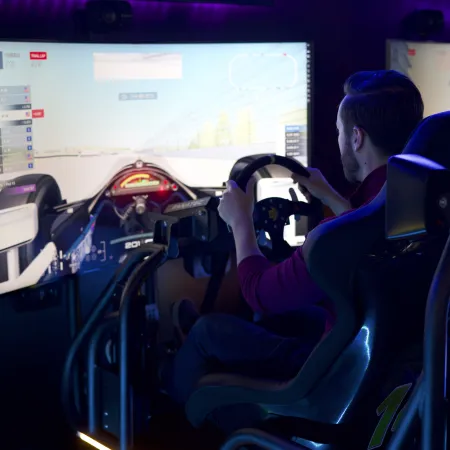 A person engages in a high-tech racing simulator, focusing intently on the screen and steering wheel.