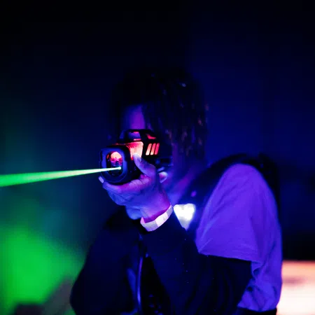 Person aiming a laser tag gun with glowing red and green lights in a dark, neon-lit environment
