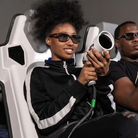 Two people wearing 3D glasses, engaged in a gaming experience, holding futuristic controllers.