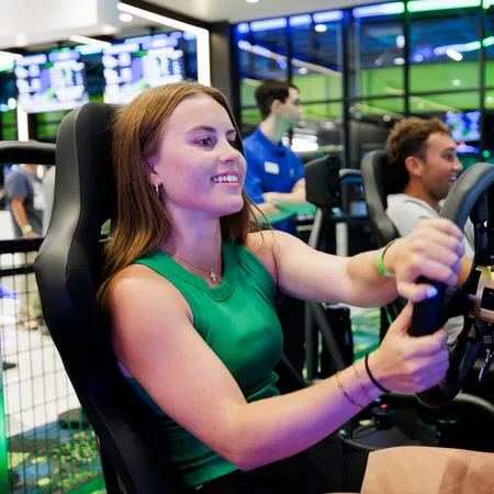 Young woman enjoying a racing simulator game with others in a bright, modern arcade setting