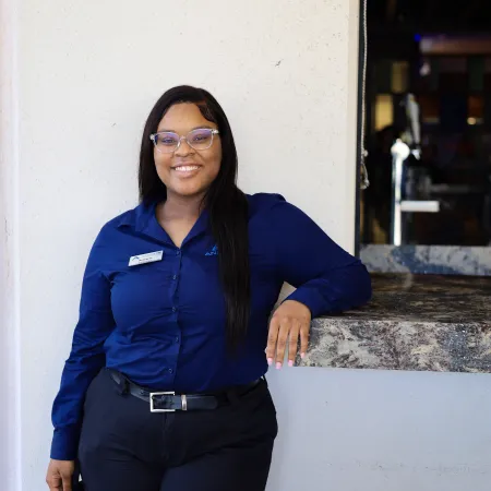 Smiling woman in a blue shirt standing by a counter, showcasing a friendly customer service atmosphere.