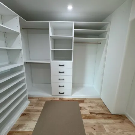 Modern white walk-in closet with open shelves, drawers, hanging rods, and natural wood flooring.