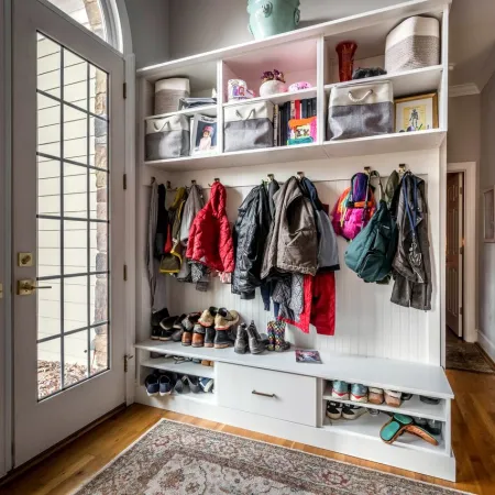 Organized mudroom with hanging coats, shelves of storage bins, shoes, and glass doors leading outside.