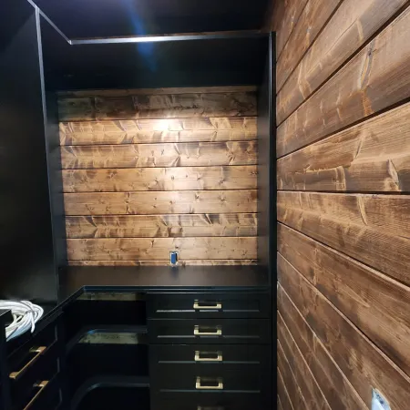 Black built-in cabinets with gold handles against rustic wooden plank walls in a small room under construction.