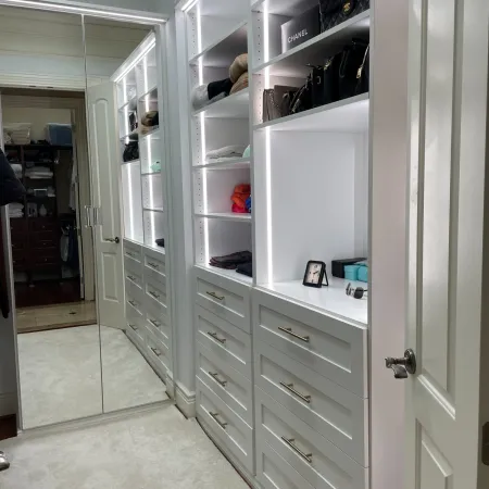 Spacious white walk-in closet with shelves, drawers, handbags, illuminated shelves, and a full-length mirror.