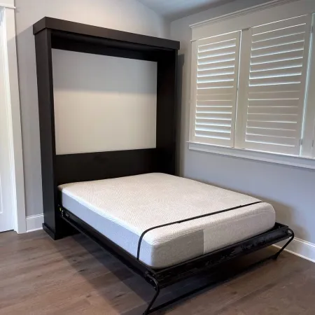 Modern wall-mounted Murphy bed with white mattress in a minimalist room with wooden floor and window shutters