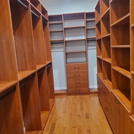 Empty walk-in closet with wooden shelves, drawers, and hanging rods on both sides and back wall.