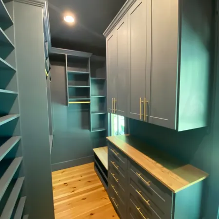 Modern gray closet with built-in shelves, gold handles, and wooden floor in a well-lit room.