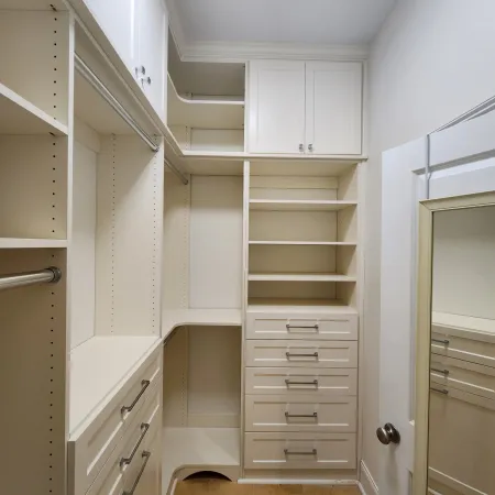 Spacious white walk-in closet with shelves, drawers, hanging rods, and a wood floor.