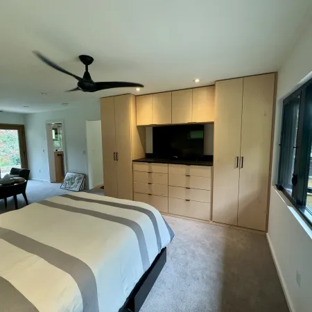 Spacious bedroom with large bed, built-in wooden wardrobe, ceiling fans, and a window overlooking a balcony.