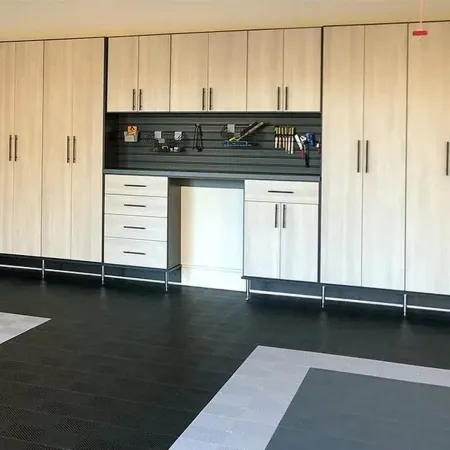 Light wood garage cabinets with black handles and integrated workspace setup with tools on pegboard.