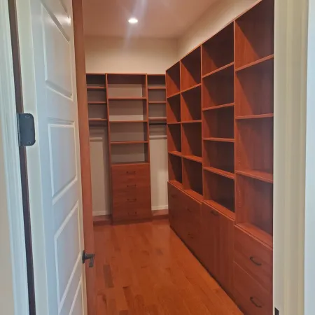 Walk-in closet with built-in wooden shelves, drawers, and hardwood flooring illuminated by recessed ceiling lights