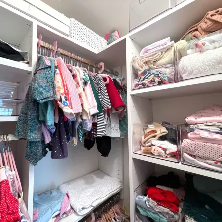 Organized small closet with hanging children's clothes and neatly folded sweaters and shirts on shelves.
