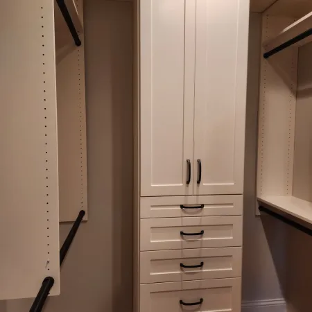 Tall white wardrobe with multiple drawers and hanging rods in a walk-in closet with wooden floor