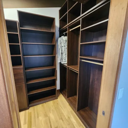 Empty wooden walk-in closet with built-in shelves and hanging rods, featuring a wooden floor and one hanging shirt.