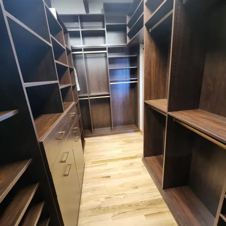 Empty walk-in closet with dark wood shelves and light hardwood flooring under bright ceiling light