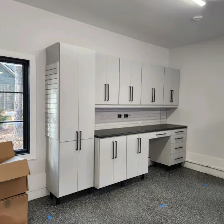 Modern white storage cabinets with black handles in a well-lit room with speckled gray flooring and window view.