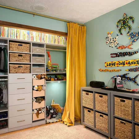 Organized kids' closet with yellow curtains, stuffed animals, wicker baskets, and colorful animal wall art on green walls.