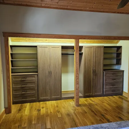 Spacious wooden wardrobe with shelves, drawers, and hanging space in a room with hardwood floors and a wood-paneled ceiling.