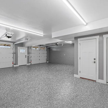 Spacious modern three-car garage with white walls, textured flooring, and two white entry doors under bright LED lighting