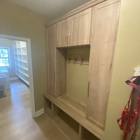Built-in wooden mudroom storage with cabinets, hooks, and cubbies in a light-colored hallway.