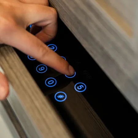 Finger pressing illuminated keypad number 8 on modern electronic device integrated into wood surface