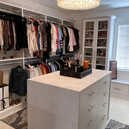 a room with a white cabinet and a white counter with a white shelf with clothes on it