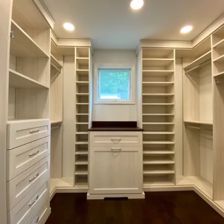 Spacious custom walk-in closet with white shelving, drawers, and dark hardwood floor under recessed lighting.
