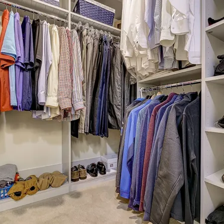 Organized walk-in closet with hanging shirts, pants, jackets, shelves with shoes, and folded clothes neatly arranged.